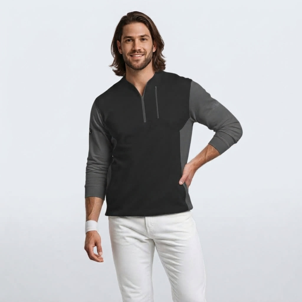 A man modeling a black and gray color-blocked long-sleeve quarter-zip pullover, paired with white pants, against a light gray studio background.